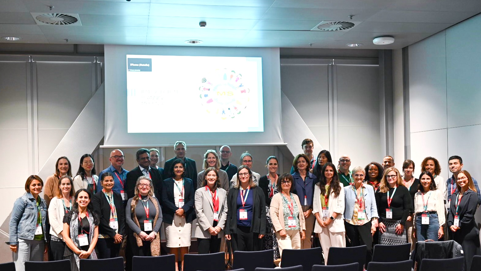 Gruppenfoto von etwa 30 Konferenzteilnehmern in einem Vortragsraum, die vor einer großen Leinwand mit einer Präsentation posieren.